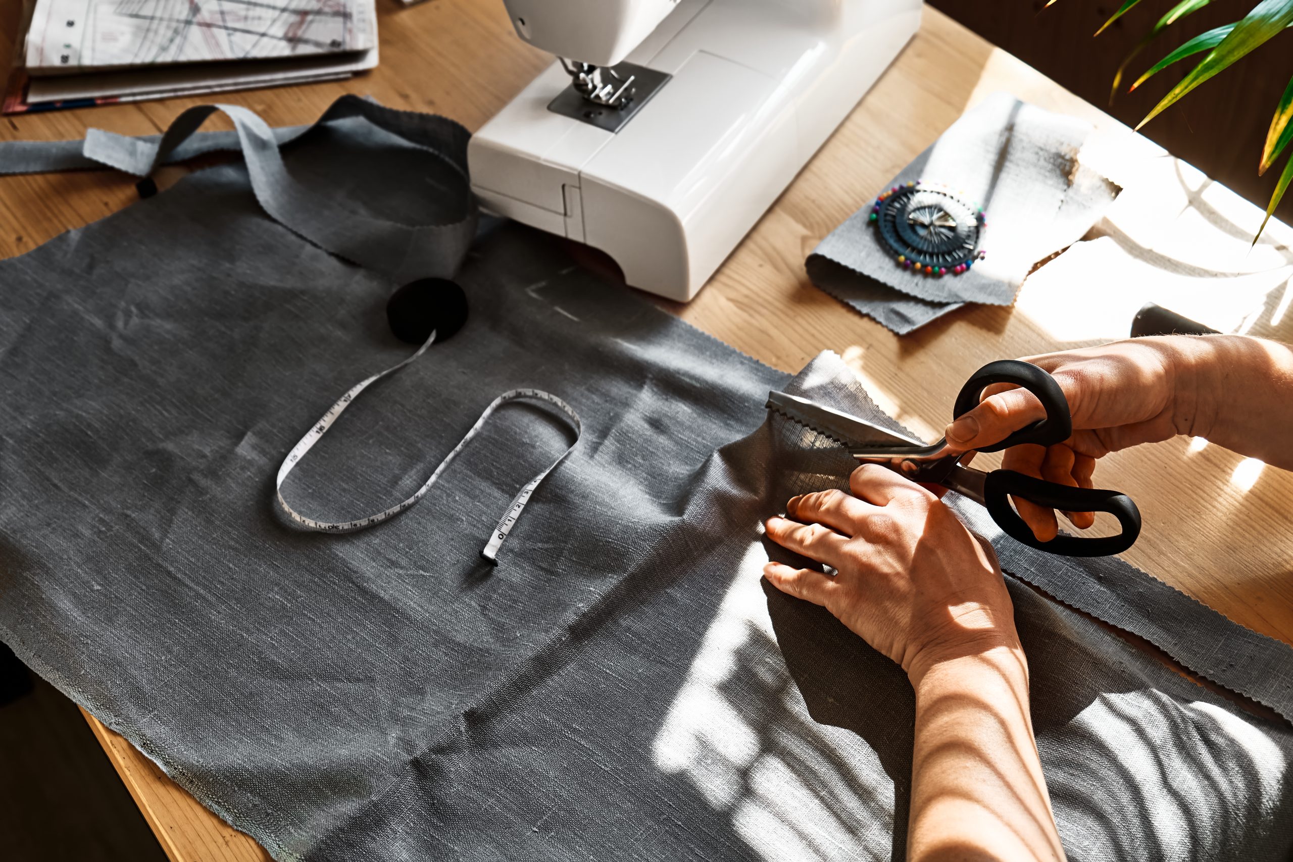 Woman cutting out a pattern paper in linen fabric. Seamstress sewing on the sewing machine in small studio. Fashion atelier, tailoring, handmade clothes concept. Slow Fashion Conscious consumption